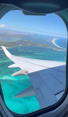 the view from an airplane window looking out at the ocean and land beyond it's wing