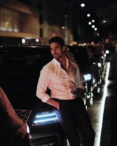 a man sitting on the hood of a car in front of some cars at night