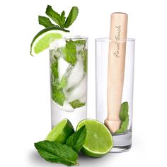 two glasses filled with ice and limes next to a wooden pepper shaker on a white background