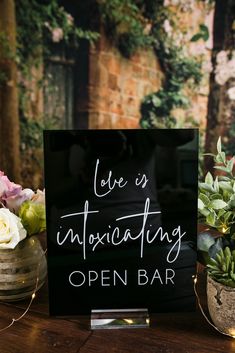 a sign that says love is intoxicating open bar next to potted plants