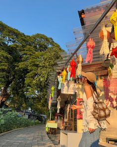 a woman standing in front of a store with clothes hanging from it's roof