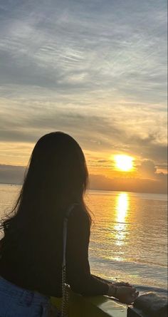 a woman sitting on top of a surfboard next to the ocean at sunset or dawn