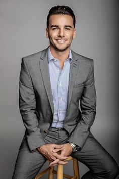 a man sitting on top of a wooden stool wearing a suit and smiling at the camera