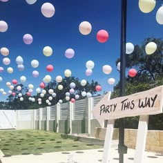 balloons are flying in the air over a yard with a sign that says party this way