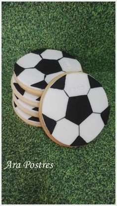 three cookies decorated with soccer balls on top of green grass, one is white and the other is black