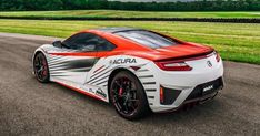 an orange and white sports car driving down a road with grass in the back ground