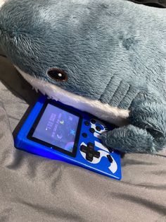 a stuffed shark laying on top of a bed next to an electronic game console controller