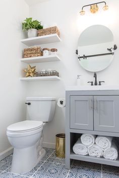 a white toilet sitting next to a sink in a bathroom under a large round mirror