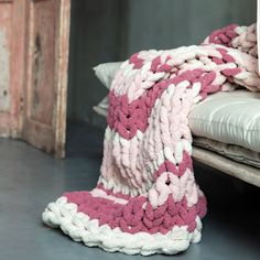 a pink and white crocheted blanket sitting on top of a bed next to pillows