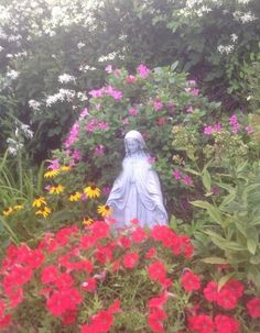 a statue surrounded by flowers and plants in the middle of a garden with red, yellow, pink and white flowers