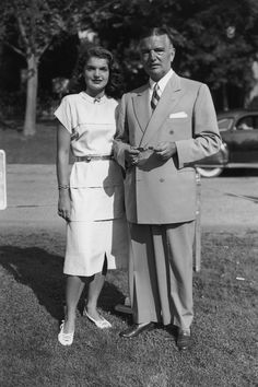 an old black and white photo of a man and woman standing in front of a car