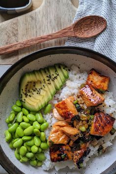 a bowl filled with rice, meat and vegetables next to a wooden spoon on top of a table