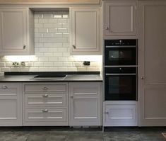 an empty kitchen with white cabinets and black counter tops on the tile floor in front of two ovens