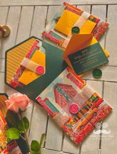 an assortment of different colored envelopes on a wooden table next to a pink rose