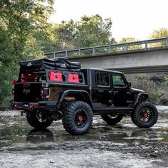 a black jeep parked on the side of a river next to a bridge and trees