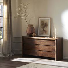 a wooden dresser sitting in front of a window next to a vase with flowers on it