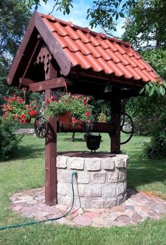 a garden well with potted plants and flowers on it's stand in the middle of a yard