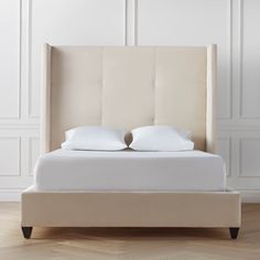 an upholstered bed with two pillows on the headboard and foot board, against a white wall