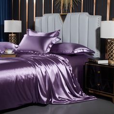 a bed with purple sheets and pillows on top of it next to two nightstands