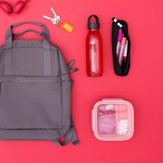 the contents of a back pack laid out on a pink surface, including water bottles and other items