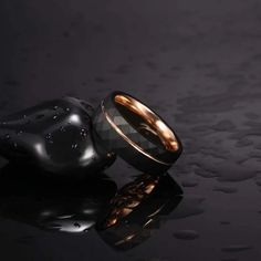 two wedding bands sitting next to each other on top of a black surface with drops of water