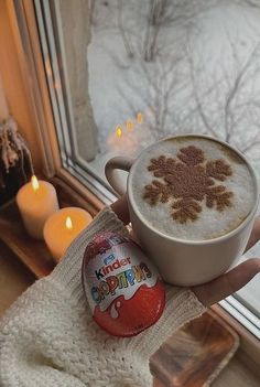 a person holding a cup of hot chocolate in front of a window