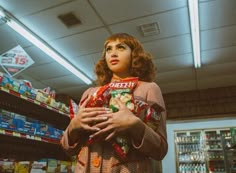 a woman standing in a grocery store holding a bag of candy and looking at the camera