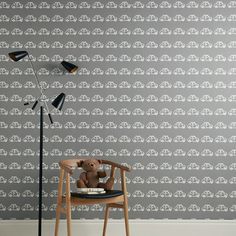 a teddy bear sitting on a chair in front of a wallpapered with cars