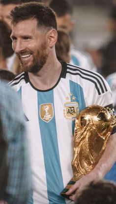 a man holding a golden soccer ball in his right hand and wearing a blue and white striped shirt