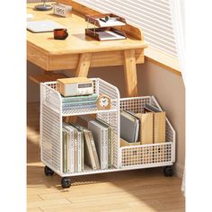 a white shelf with books and magazines on it in front of a wooden table next to a window