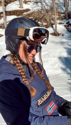 a woman sitting in the snow wearing a helmet and goggles on her head,