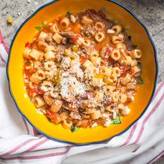 a yellow bowl filled with pasta and meat on top of a white towel next to a fork