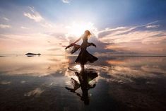 a woman is dancing on the beach at sunset