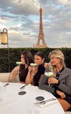 three women sitting at a table with drinks in front of the eiffel tower