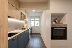 a narrow kitchen with blue cabinets and white counter tops, along with hardwood flooring