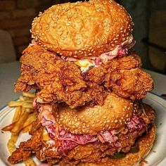 a stack of fried chicken sandwiches on top of a white plate with french fries and ketchup