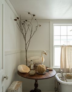 a white bath tub sitting next to a wooden table in a bathroom with a bird statue on top of it