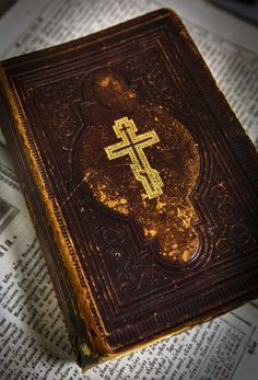 an old book with a cross on it sitting on top of a table next to a pen