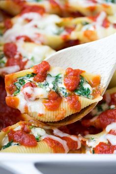 stuffed shells with sauce and spinach being held by a spatula in a white casserole dish