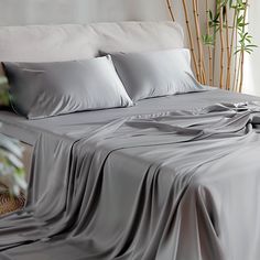 a bed covered in grey sheets and pillows