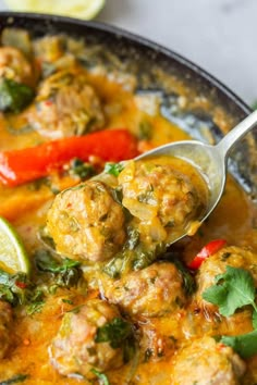 a spoon full of meatballs and vegetables in a curry sauce with lime wedges