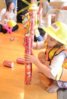 a group of children sitting around a table with construction hats on and holding up cans