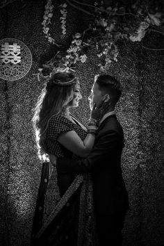 a man and woman standing next to each other in front of a wall with flowers on it