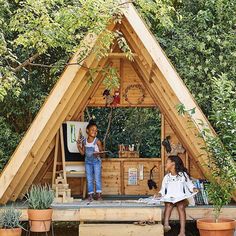 two people are sitting in front of a small wooden structure that is made out of wood