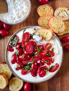 a bowl filled with yogurt and cherry tomatoes next to bread on a wooden table