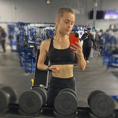 a woman standing in a gym holding a cell phone