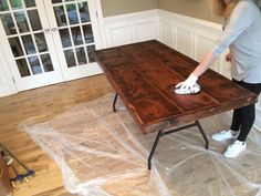 a woman is cleaning a wooden table in the middle of a room with plastic covering it