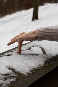 a person's hand reaching for the snow on top of a bench in winter