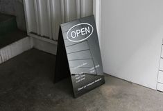 an open sign sitting in front of a white wall next to a black and silver door