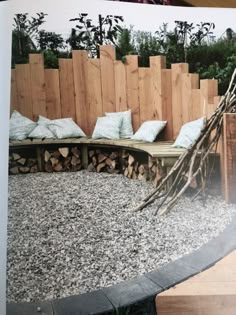 an outdoor seating area made out of wood and rocks with pillows on it, surrounded by wooden fence